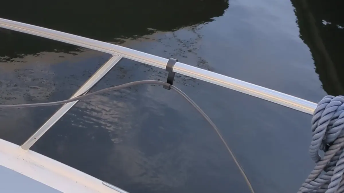 Ein schwarzer Relinghaken aus robustem Kunststoff hält ein schwarzes Landstromkabel sicher an einer weißen Bootsreling über dem Wasser. Der Haken dient als praktische Kabelführung und Ordnungssystem an Bord, um Stolperfallen zu vermeiden.