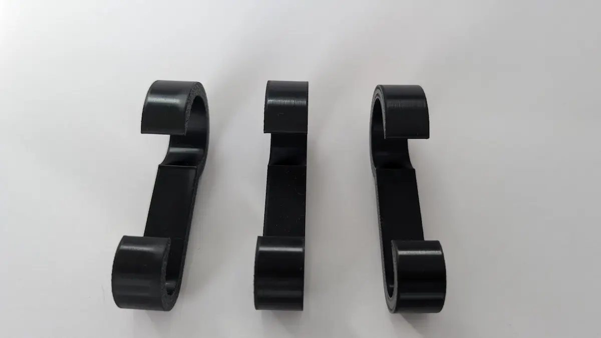 in Set aus drei schwarzen Kunststoff-Relinghaken, die an der Bootsreling befestigt sind und ein aufgewickeltes orangefarbenes Landstromkabel sicher halten.