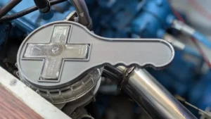 Ein grauer, kreuzförmiger Kunststoff-Schlüssel liegt passgenau auf dem Deckel eines Seewasserfilters im Motorraum eines Bootes. Das Werkzeug dient zum leichten Öffnen und Schließen des Filters ohne Beschädigung.