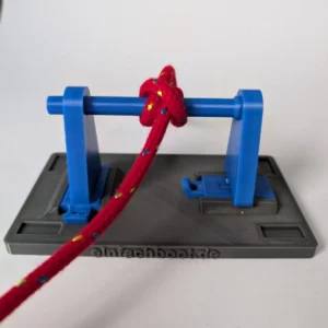 Ein funktionales Knotenbrett-Modul bestehend aus einer grauen Basisplatte und einer aufgesteckten blauen Reling. Ein rotes Seil ist mit einem Webleinsteg (Mastwurf) an der Reling befestigt, um die Nutzung als Übungsboard für Seemannsknoten zu demonstrieren.