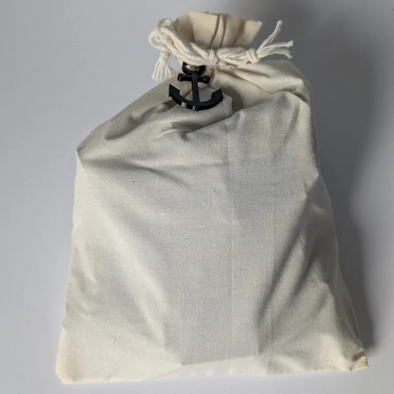 Hochwertige Geschenkverpackung für das Knotenbrett: Ein cremefarbener Baumwollbeutel mit Kordelzug, verziert mit einem kleinen schwarzen Deko-Anker.